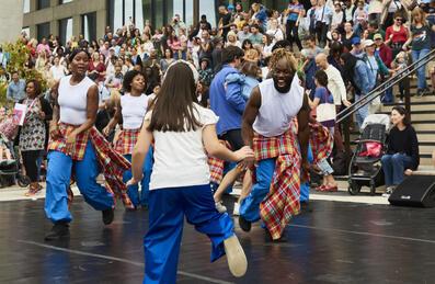 A group of dancers on stage with the crowd behind