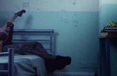 Hak Baker sits on a bed with a guitar
