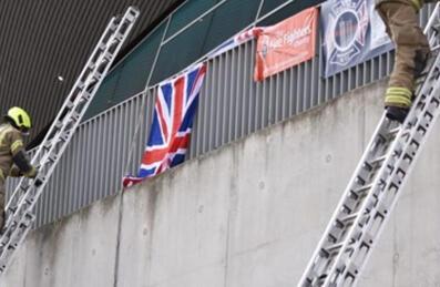Two firefighters in full gear climb up ladders