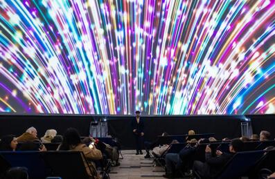 A large planetarium screen lights up with people sat beneath