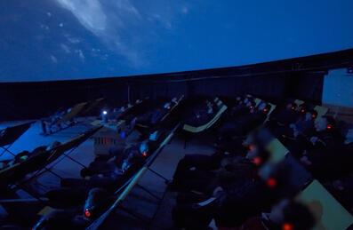 A dark planetarium filled with people looking up at the ceiling.
