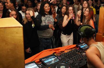A crowd of people dance in front of a DJ decks