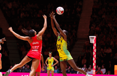 Two competing netball teams in yellow and pink jerseys play on the court.