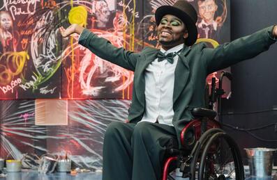 A person in a wheelchair celebrates in front of a painting