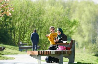 Women and her daughter sitting on a bench at Queen Elizabeth Olympic Park on a sunny day