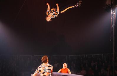 A circus acrobat is thrown high in the air with spotters beneath them