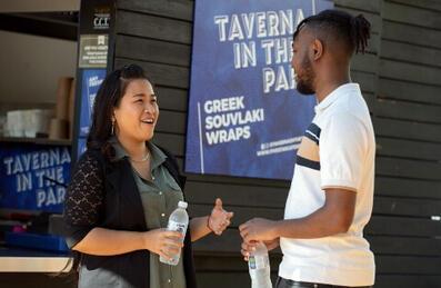 A man and woman chatting outside a food kiosk called Taverna in the Park