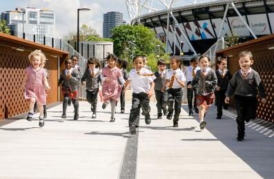 Young children running across a bridge in front of London Stadium