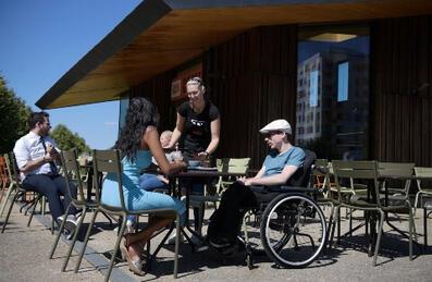 A man in a wheelchair having coffee with a woman in a blue dress.