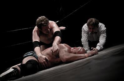 2 men wrestling, 1 lying on ground with referee in background