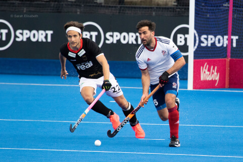 Two hockey players run with one in control of the ball
